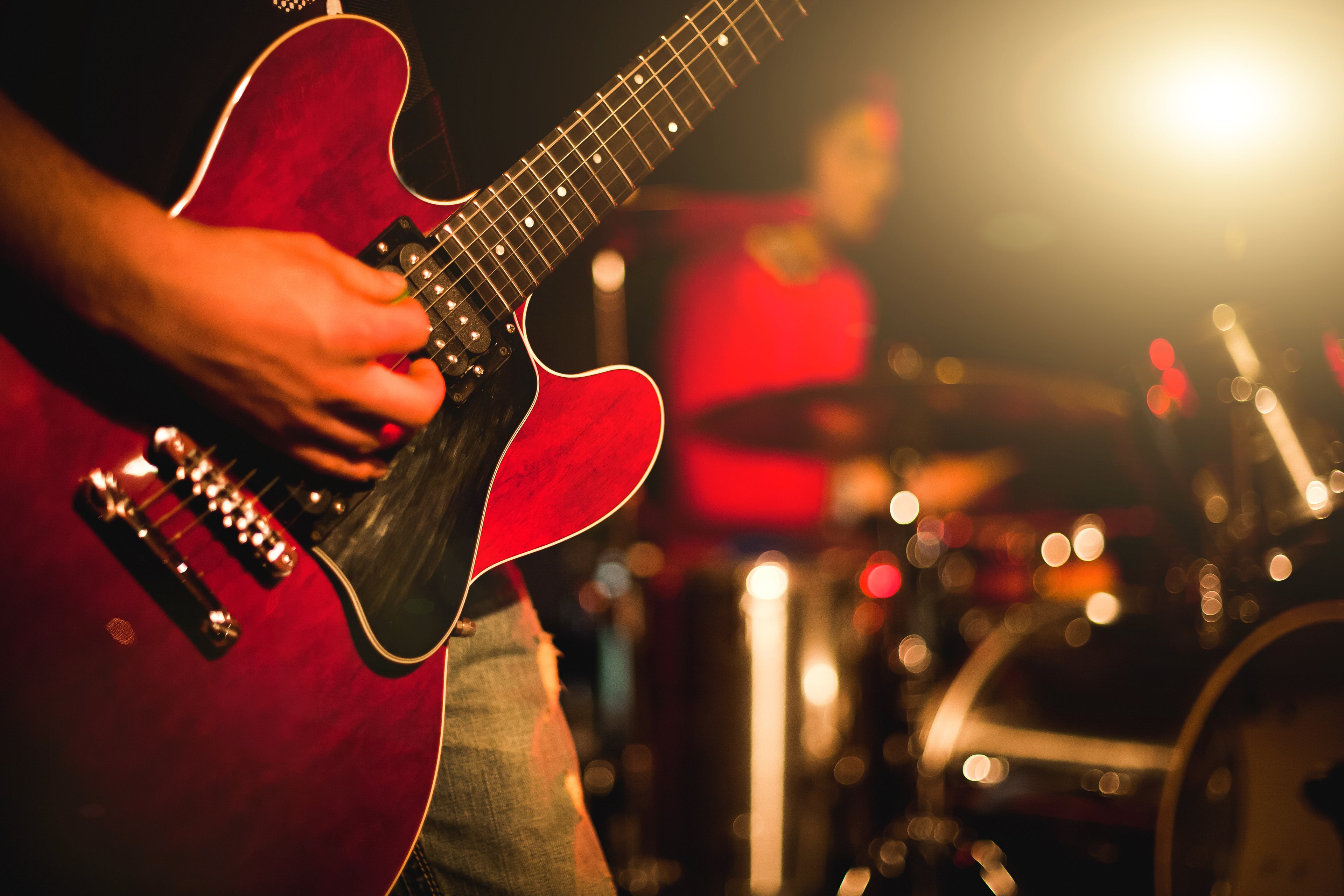 Man on stage playing red electric guitar